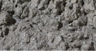 Detailaufnahme von grobkörnigem, feuchtem Frischbeton. Die Oberfläche ist uneben und zeigt die typischen Strukturen und Glanzstellen von noch nicht ausgehärtetem Beton